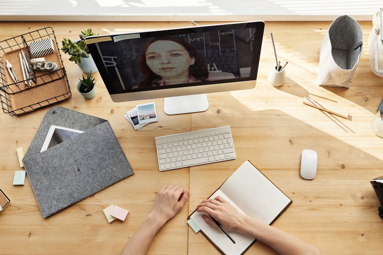 An overhead view of a modern home office setup for online learning and virtual meetings, featuring a desktop computer and notepad.